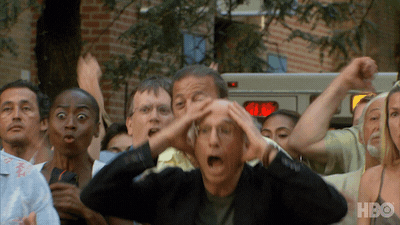 TV gif. Larry David on Curb Your Enthusiasm stands among a cheering crowd with an expression of jaw-dropped shock, then high fives the man standing next to him.
