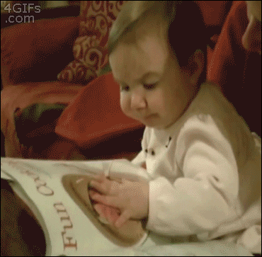 Video gif. A baby is holding an open magazine and staring at a picture of soup. They put their fingers to the picture and put it in their mouth, acting as if they're eating the soup in real life.
