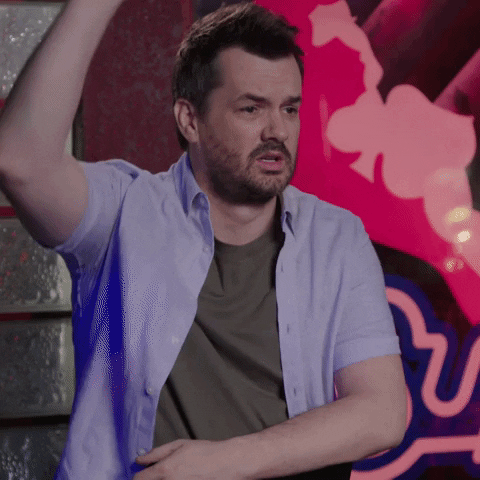 Reality TV gif. Jim Jefferies on the Jim Jefferies Show raises his hand and he looks around with a concerned look on his face as he says, “I’m gonna say yes.”
