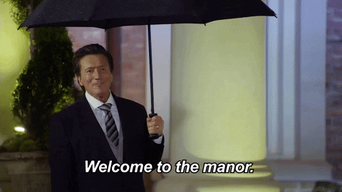 Reality TV gif. Martin Andrew as The Butler on Joe Millionaire: For Richer or Poorer. He greets contestants as they walk in, holding an umbrella open and saying, "Welcome to the manor."