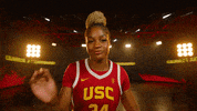 Promo gif. Clarice Akunwafo, a USC women's basketball player swipes at the camera and gives a sassy look as she turns around to walk away. Behind her is a set with stage lights and giant floor-to-ceiling curved TVs. 