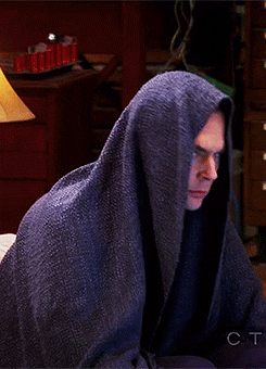 Big Bang Theory gif. Jim Parsons as Sheldon sits with a blanket wrapped around his face. He  lifts his head up to look at whoever's talking and is clearly upset at whatever they've said.