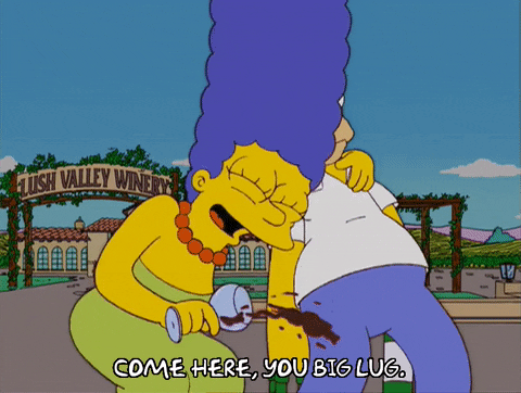 The Simpsons gif. Marge and Homer Simpson outside the Lush Valley Winery, Marge holding a wine glass and Homer with wine bottles stuck on the ends of his fingers, both of them drunk. Marge says, “Come here, you big lug,” before wrapping her arms around Homer and lowering him into a deep kiss.