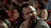 Late Night gif. Aaron Paul sits in a theater with others, looking peeved while frowning, shaking his head, and scratching his mouth before shouting "booooo, bitch."