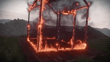Music video gif. A scene from Petit Biscuit's music video where the frame of a home is on fire. The flames lick the wood and black smoke spits out as the house sits in an agricultural field.