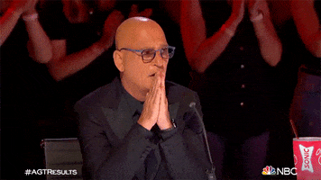 Reality TV gif. Howie Mandel of America's Got Talent watches intently while pressing his hands together in front of his face, in hope or suspense.