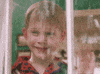 Movie gif. Macaulay Culkin as Kevin from Home Alone waves out a window as snow falls outside.