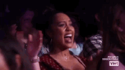 Reality TV gif. Audience members of RuPaul's Drag Race clapping and getting hyped up while smiling.