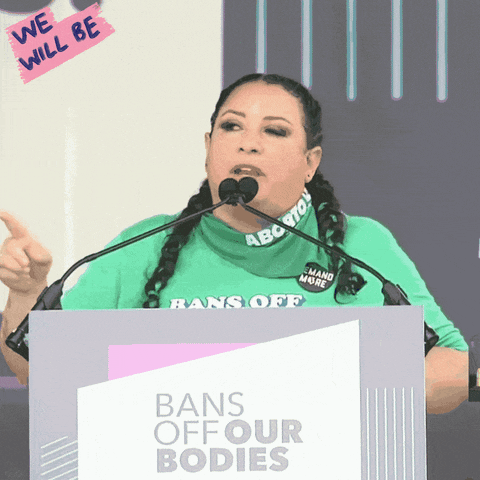 Video gif. Woman wearing a bright green t-shirt speaks emphatically at a podium above a sign that reads, "Bans off our bodies." She says, "We will be ungovernable until this government starts working for us."