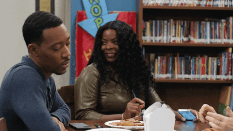 TV gif. Janelle James as Ava and Tyler James Williams as Gregory in Abbott Elementary. He sighs at her as she cackles and tosses her hair back before falling off her seat.