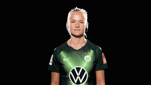 Sports gif. Pernille Harder looks straight at us, then turns to her right, smiles, and points upward with both hands. 