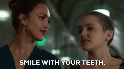 TV gif. Jessica Alba as Detective Nancy from L.A.'s Finest tells Sophia Reynolds as Isabel McKenna to "Smile with your teeth," and provides a huge, teethy smile to demonstrate.