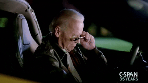 Political gif. Joe Biden sits in a sports car wearing a leather jacket, puts on aviator sunglasses, puts the car in reverse, and starts to drive off.