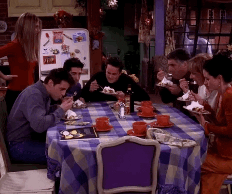 Friends gif. Jennifer Aniston as Rachel stands and watches her friends sit around a table eating a whipped dessert apprehensively.