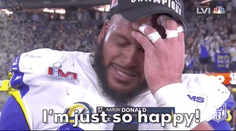 Sports gif. Aaron Donald scratches his forehead and appears emotional as he speaks into a microphone, "I'm just so happy!"