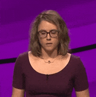 Video gif. Contestant on a game show shakes her head while hesitantly trying to figure out an answer to a question.