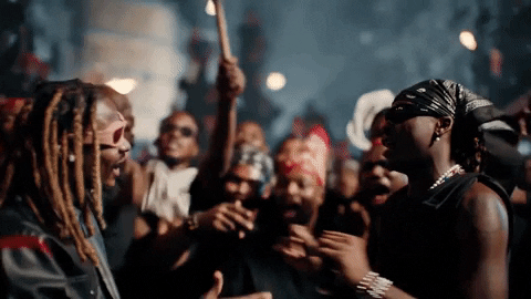 Video gif. An crowd surrounds two men with torches. The two men hug and the crowd cheers excitedly.