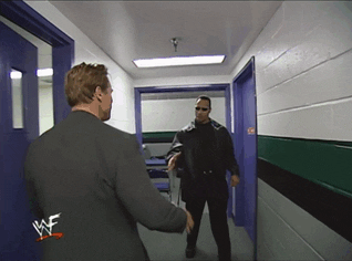Celebrity gif. Dwayne Johnson, sharply dressed in all black with snazzy shades and sideburns, firmly shakes hands with a smiling Arnold Schwarzenegger.