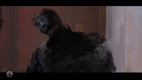 SNL gif. Body of a man is charred and burned to a crisp. Smoke comes off of the burnt body.