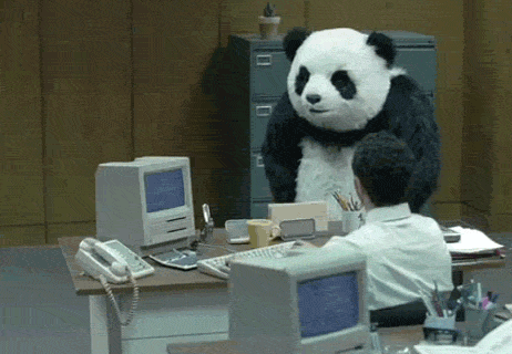Video gif. A person in a panda costume sweeps everything off a desk as the man sitting at it shifts back.