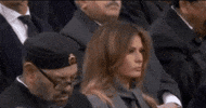 Political gif. Melania Trump holds a forward gaze as we scan to Donald Trump beside her, scowling at her with a dirty look.