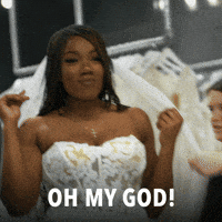 Reality TV gif. Paige Banks from Married at First Sight is trying on her wedding dress for the first time and she's glowing. She looks at her reflection and says, "Oh my god! Who is she?"
