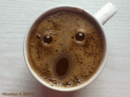 Video gif. We look down into a cup of coffee as frothy bubbles turn into a face that winks at us. 