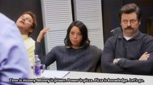 Parks and Recreation gif. Aubrey Plaza as April waves her hand in the air, sitting at a table next to Nick Offerman as arms-crossed Ron Swanson, and says, "Time is money, money is power, power is pizza, pizza is knowledge, let's go" which appears as text.