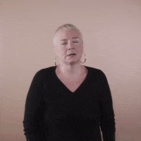 Reaction gif. A white woman with invisible disabilities, with hair styled in a sleek platinum pixie cut and big hoop earrings drops her head back, eyes closed, then looks at us with exasperation in her eyes and says, "Tired."