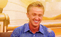 Celebrity gif. Tom Felton is being interviewed but something makes him laugh big time and he covers his mouth with both hands as he cracks up.
