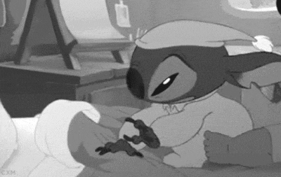 Disney gif. Stitch from Lilo & Stitch in his pajamas and nightcap pulls his doll from under his pillow, snuggles into bed.