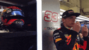 Sports gif. Max Verstappen of Red Bull's Formula One racing team is in his uniform and is preparing for a race, heating up his earbuds in his hands as his helmet sits next to him.