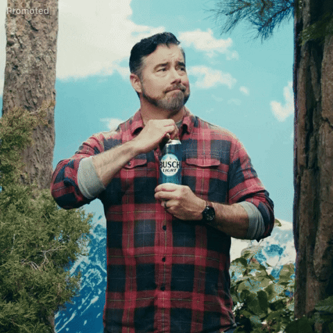 Sponsored gif. Gerald Downey looks around with a content expression standing among pine trees and snowcapped mountains in the distant background. He cracks a can of beer as a deer, owl, and squirrel pop into frame as Downey looks at us with confused acceptance. Text, "Sounds like happy hour."
