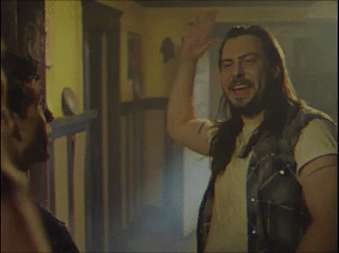 Movie gif. Andrew W.K. as Rip Stick in Dude Bro Party Massacre III excitedly throws a high five into the air toward another guy as he yells “Yay!” The high-five turns into a hand hug mid-air as the hands clasp each other.