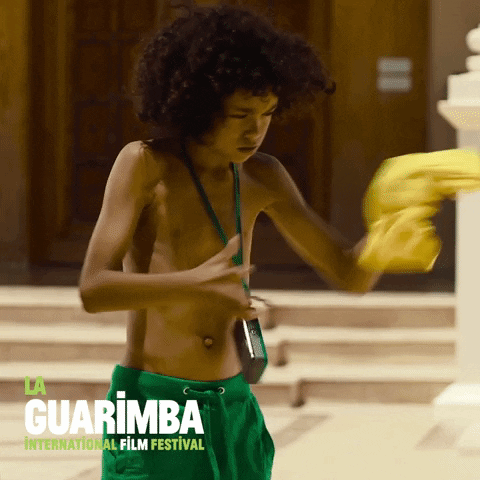 Video gif. A young boy without a shirt on wads a shirt up into a ball and throws it as hard as he can at us. 