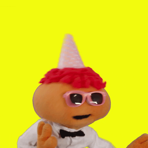 Video gif. Gerbert the puppet wears a party hat, pink sunglasses, and a bowtie, dancing in celebration as confetti rains down against a lemon yellow background.