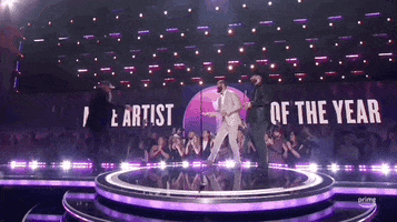 Academy of Country Music Awards gif. Chris Stapleton walks on stage and shakes the hands of the award presenters awaiting him. The words in the background read "Male Artists of the Year". As one presenter hands Stapleton the throphy, the other walks off the stage as if his job his done. Chris holds appreciative demeanor.