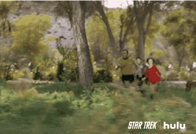 TV gif. William Shatner as Captain Kirk on Star Trek runs fast with two other crew members through the woods.
