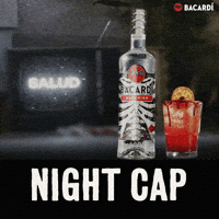 Sponsored gif. A Halloween-themed bottle of Bacardi and an orange cocktail on a counter next to a staticky old fashioned television set. The tv screen reads" SALUD" Text: "NIGHT CAP"