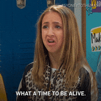 TV gif. Ava Kolker as Olive shakes her head and scrunches her nose as she says, “What a time to be alive.”