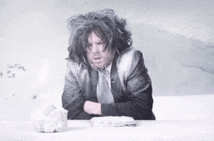 Video gif. A man in a business suit is stuck hips down in snow during a blizzard. His hair is messy and dusted with snow, ice forming on his beard. Snow pummels him as he shivers intensely.
