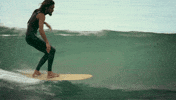 Sports gif. Surfer gracefully rides a curly wave and holds his arms out for balance.