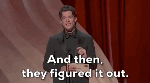 Oscars 2024 gif. John Mulaney wears a full black suit onstage. He shakes his head while saying, "And then, they figured it out."