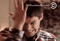 Movie gif. Jim Carrey as Lloyd in Dumb and Dumber grits his teeth and winces as he hits himself repeatedly on his head with his hand. 