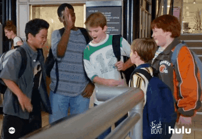 TV gif. A group of middle schools boys from the show Fresh off the Boat gathers in a school hallway, smiling and high-fiving one another happily.