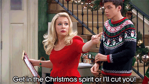TV gif. Melissa Joan Hart from Melissa & Joey wears a red Christmas dress holds up a clipboard as she aggressively points and shouts at someone offscreen. Nick Robinson rolls up the sleeve of his sweater, maybe feeling a bit awkward. Text, “Get in the Christmas spirit or I’ll cut you!”