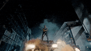 Celebrity gif. In the Car Bandana music video, Fireboy DML stands atop a black car in the nighttime city streets and sings as flames and smoke billow around him.