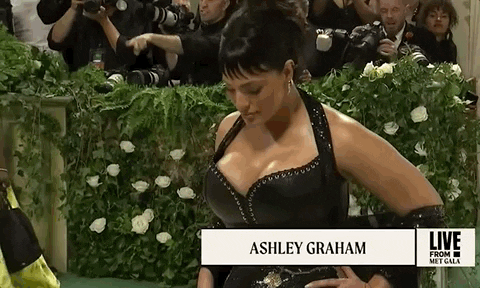 Met Gala 2024 gif. Snap-zoom out and back in on Ashley Graham posing for all angles, wearing a custom Ludovic de Saint Sernin gown with black leather bodice and sheer beaded skirt.