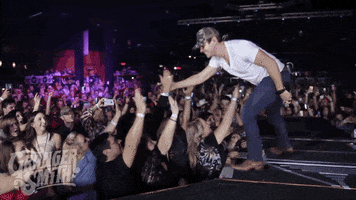 Celebrity gif. Granger Smith is onstage at his concert and he high fives people in the audience.