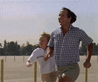 Movie gif. In a scene from National Lampoon's Vacation, Chevy Chase as Clark Griswold and Anthony Michael Hall as his son Rusty run joyously in slow motion across an empty parking lot. You can almost hear "Chariots of Fire" playing in the background.